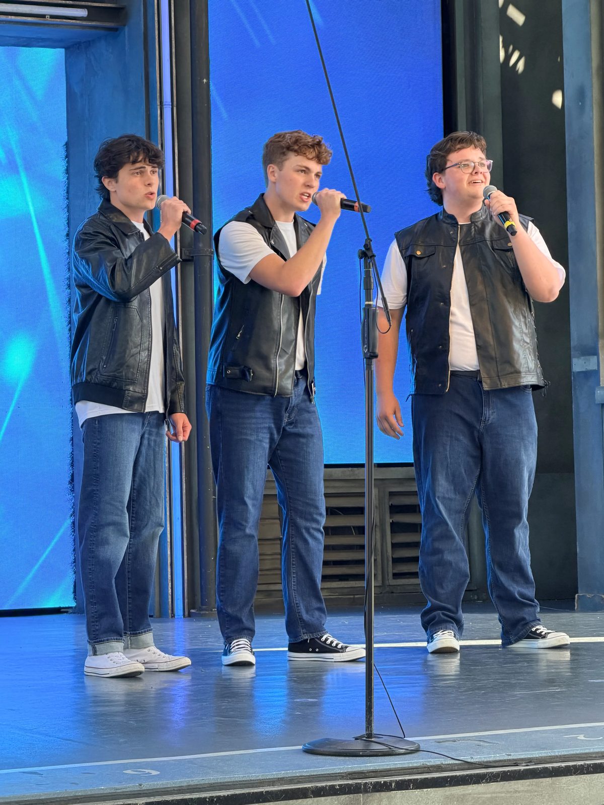 A trio of Aspire Young Artists singing at a shared microphone stand