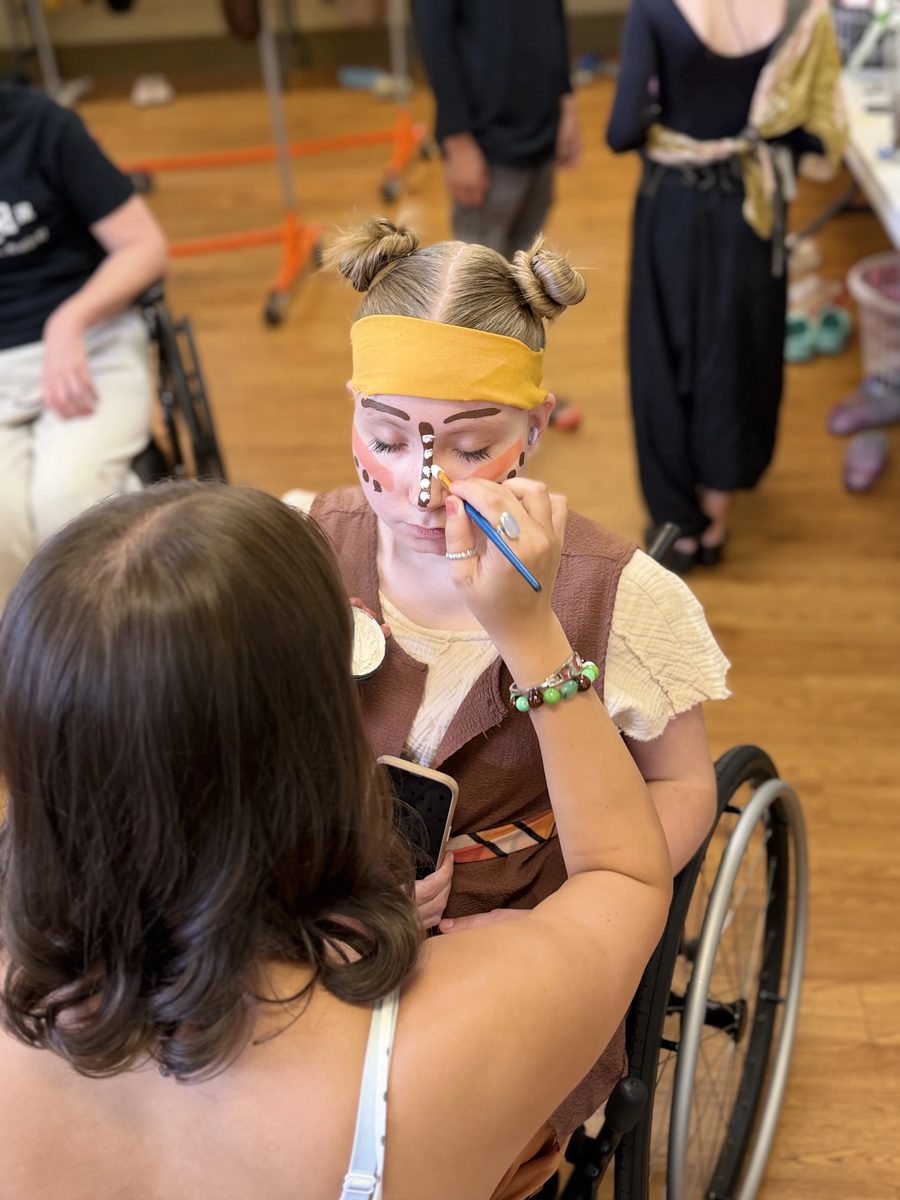 A makeup volunteer adds detail work to a Young Artist&rsquo;s face