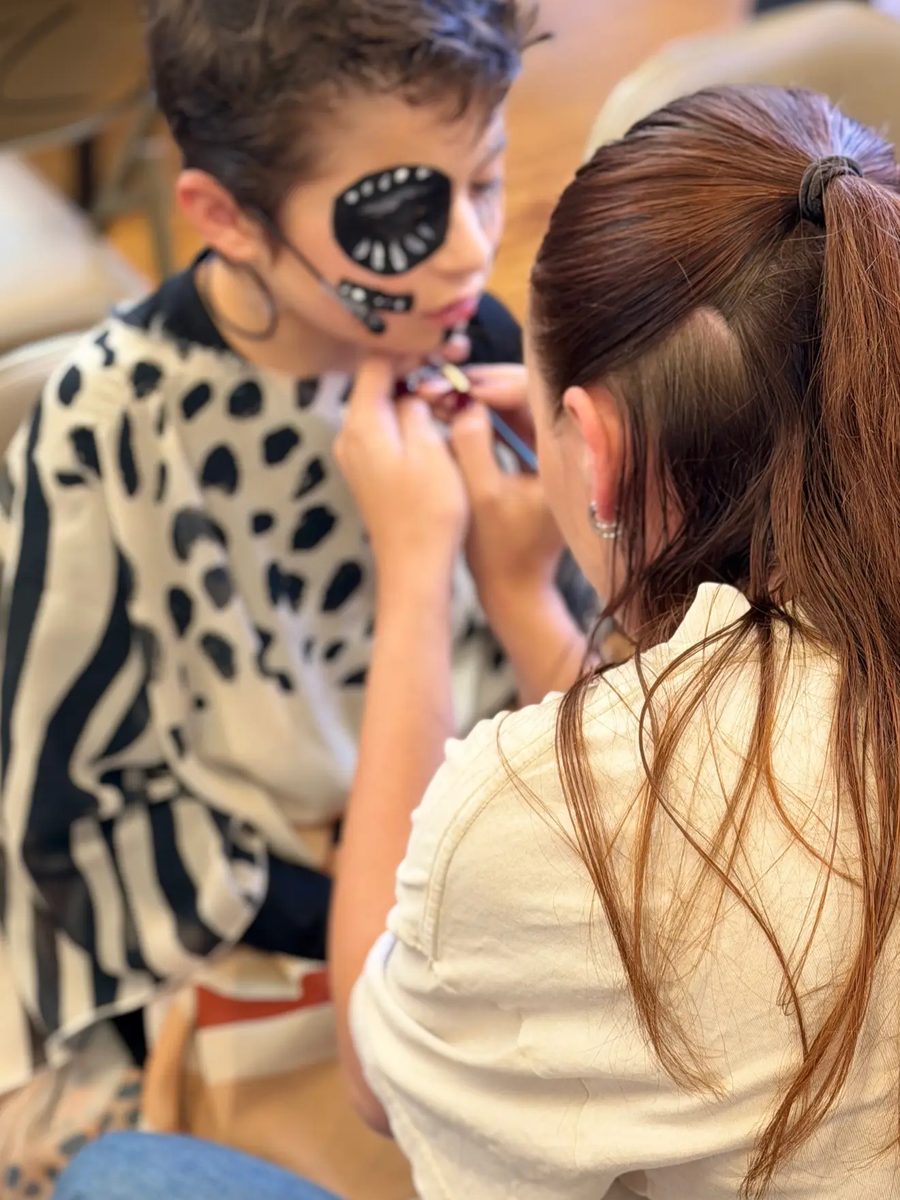 A volunteer paints hyena makeup on a Young Artist backstage