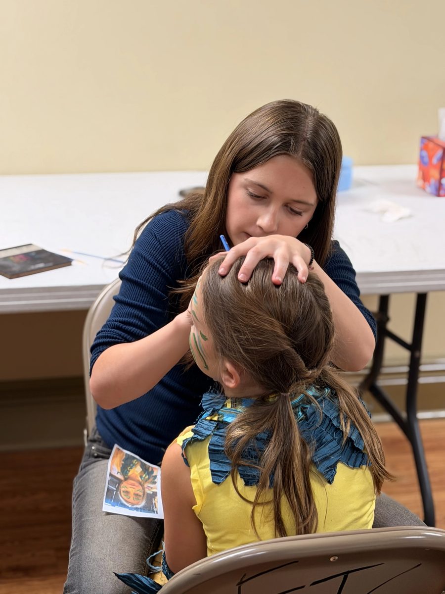 A volunteer paints leaf designs on a young castmate&rsquo;s face