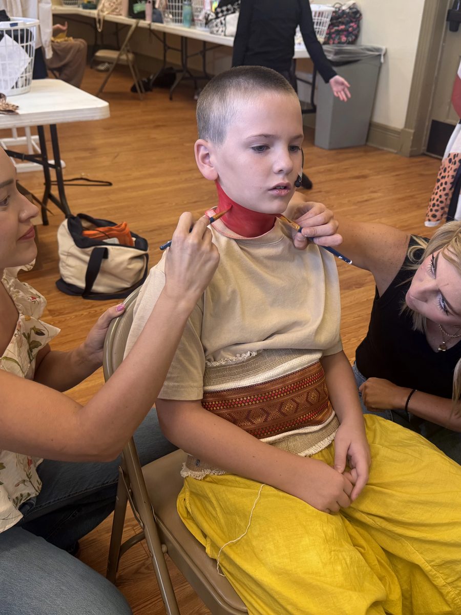 Two volunteers paint costume makeup on a Young Artist