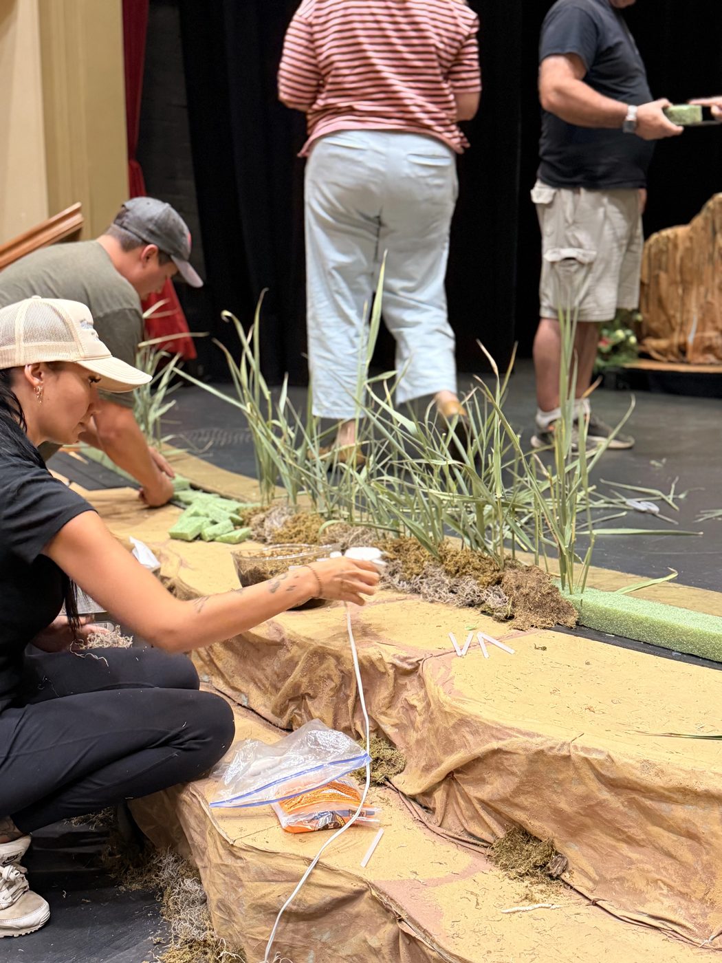 Volunteers plant savanna grasses along the front edge of the stage