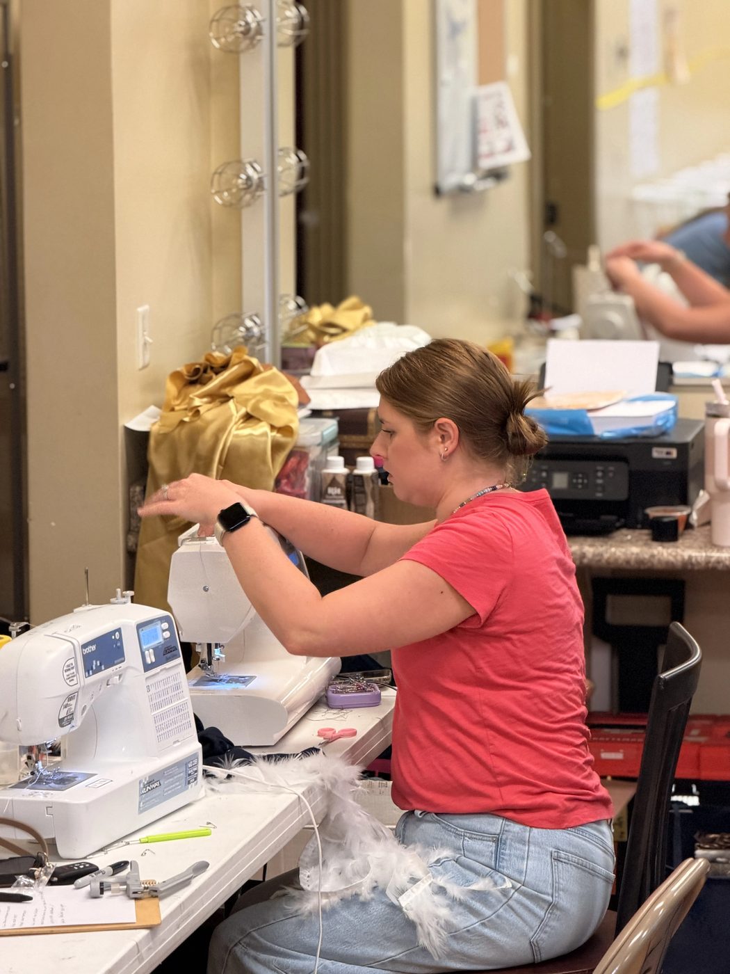 A volunteer sews costume pieces at a pair of sewing machines backstage