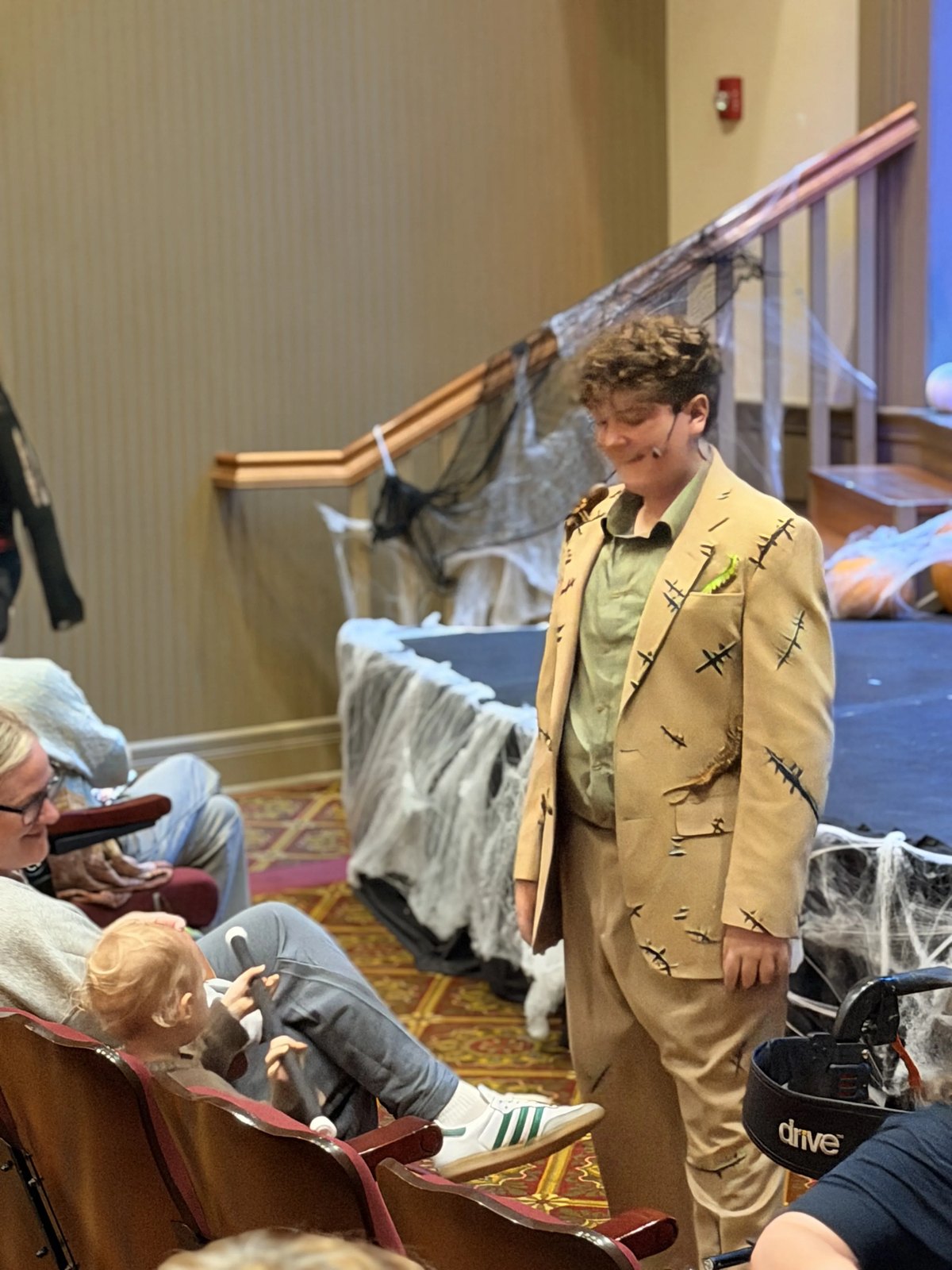 An Encore Young Artist in a stitched tan suit leaning in to say hello to a small guest seated in the audience