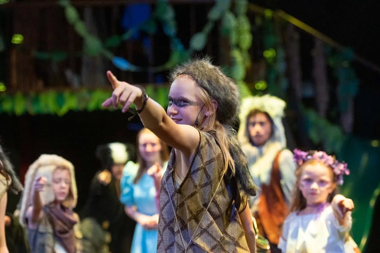 A young performer as a Lost Boy in Encore's Peter Pan, pointing across Neverland